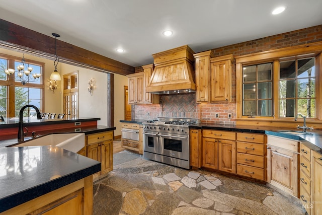 kitchen with a notable chandelier, premium range hood, range with two ovens, hanging light fixtures, and sink