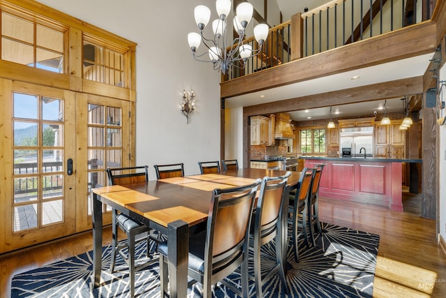 dining room featuring french doors, an inviting chandelier, hardwood / wood-style floors, a towering ceiling, and sink