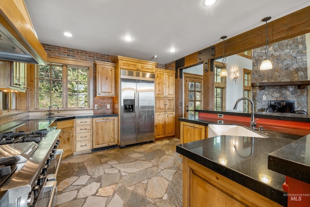 kitchen with a stone fireplace, sink, hanging light fixtures, custom exhaust hood, and premium appliances