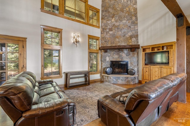 living room with a stone fireplace, light hardwood / wood-style flooring, and a high ceiling