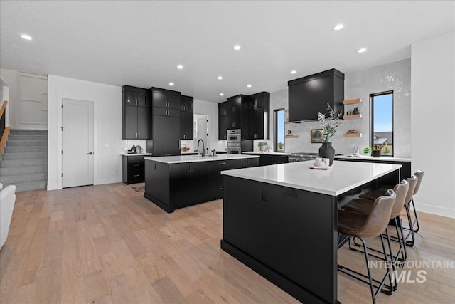 13625 Hickory Rnch, Nampa, ID 83651 - kitchen with a large island with sink, dark cabinetry, a sink, stainless steel double oven, and recessed lighting