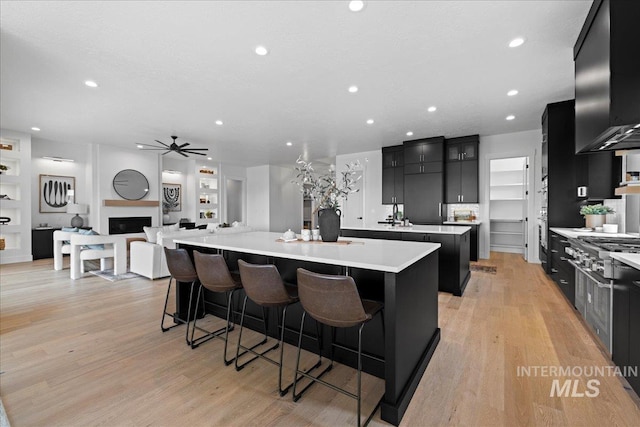 13625 Hickory Rnch, Nampa, ID 83651 - kitchen with a large island, dark cabinets, a ceiling fan, light countertops, and wall chimney exhaust hood