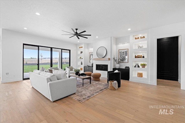 13625 Hickory Rnch, Nampa, ID 83651 - living room with built in shelves, light wood-type flooring, a ceiling fan, a textured ceiling, and a glass covered fireplace