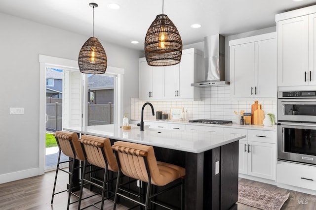 kitchen with wall chimney range hood, appliances with stainless steel finishes, decorative backsplash, wood finished floors, and recessed lighting
