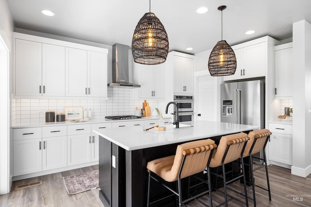 kitchen with wall chimney range hood, a sink, wood finished floors, light countertops, and recessed lighting