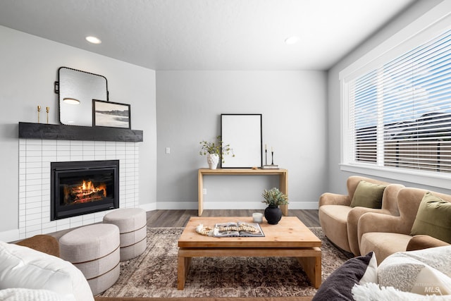 living room with wood finished floors, a tiled fireplace, recessed lighting, and baseboards