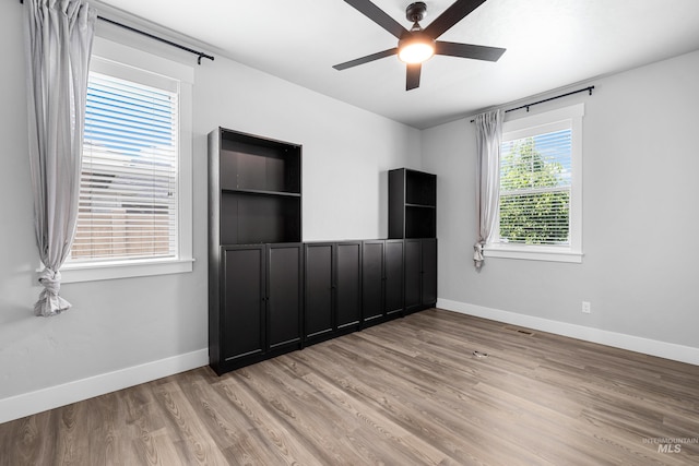 empty room with a ceiling fan, light wood-style floors, and baseboards