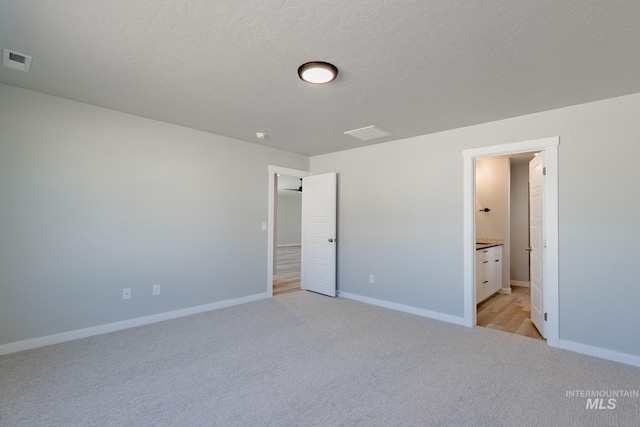 unfurnished bedroom featuring light carpet, a textured ceiling, and ensuite bathroom