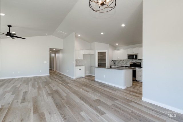 kitchen with white cabinets, appliances with stainless steel finishes, lofted ceiling, backsplash, and a center island with sink