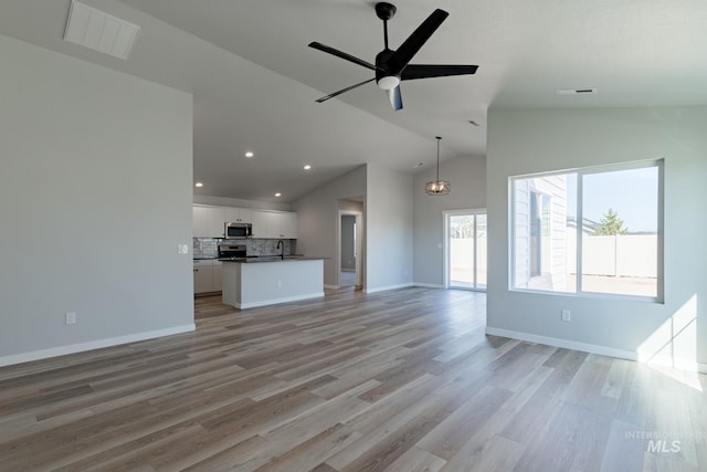 unfurnished living room featuring ceiling fan with notable chandelier, lofted ceiling, and light wood-type flooring