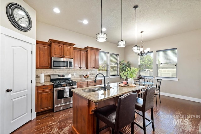 730 N Finsbury Way, Star, ID 83669 - kitchen featuring appliances with stainless steel finishes, dark wood-type flooring, decorative backsplash, a kitchen island with sink, and light stone countertops