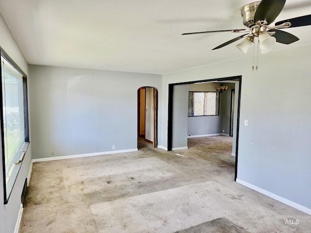empty room featuring arched walkways, carpet flooring, a ceiling fan, and baseboards