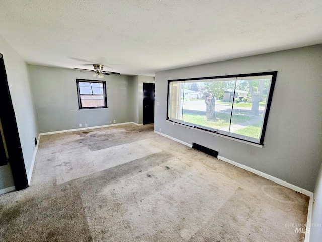 carpeted empty room featuring baseboards, a ceiling fan, and a textured ceiling