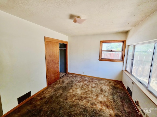 unfurnished bedroom with carpet flooring, a closet, a textured ceiling, and baseboards