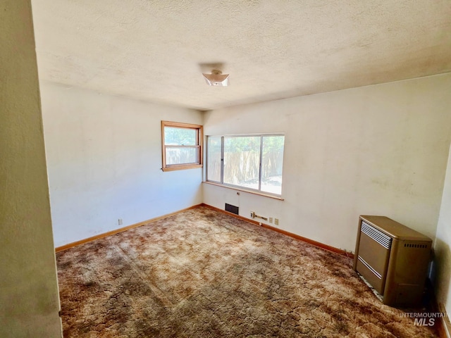 empty room with heating unit, carpet floors, baseboards, and a textured ceiling