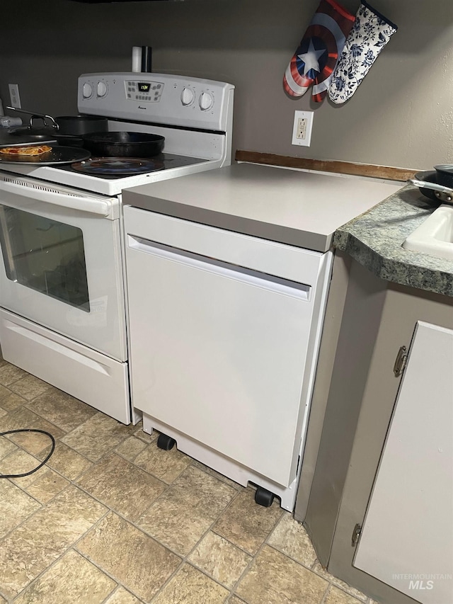 kitchen featuring dishwashing machine, electric range, stone finish floor, and white cabinetry