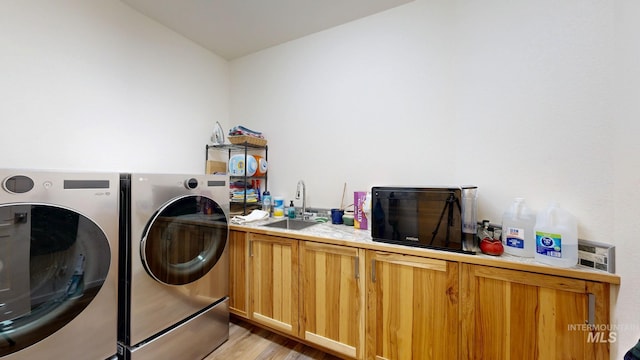 laundry room featuring light wood-style floors, washing machine and dryer, a sink, and cabinet space