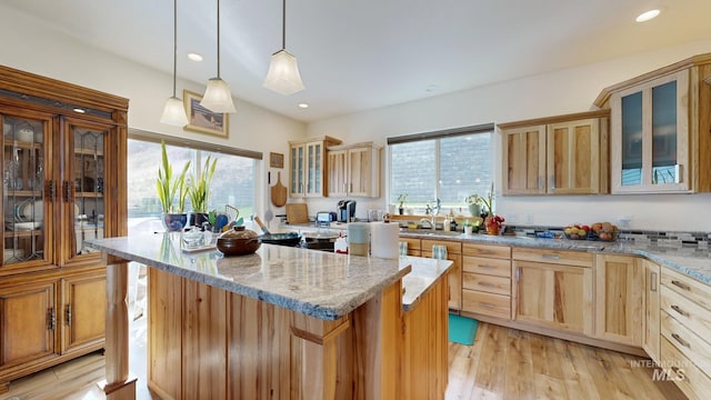kitchen featuring glass insert cabinets, a center island, light stone countertops, light wood-style floors, and light brown cabinetry