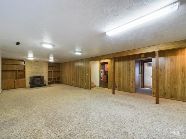 basement featuring wood walls, a textured ceiling, a wood stove, carpet floors, and built in features