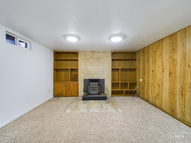 unfurnished living room with built in shelves, light colored carpet, a wood stove, and wood walls