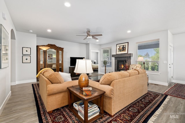 living room featuring a tile fireplace, ceiling fan, and wood-type flooring