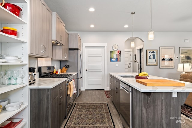 kitchen with stainless steel appliances, an island with sink, pendant lighting, dark hardwood / wood-style floors, and sink