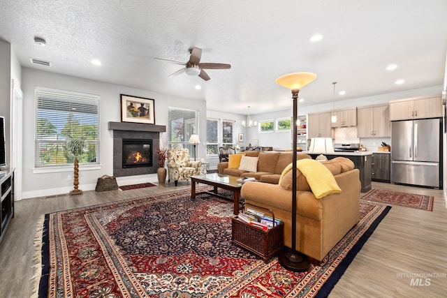 living room featuring ceiling fan with notable chandelier, a textured ceiling, light wood-type flooring, and plenty of natural light