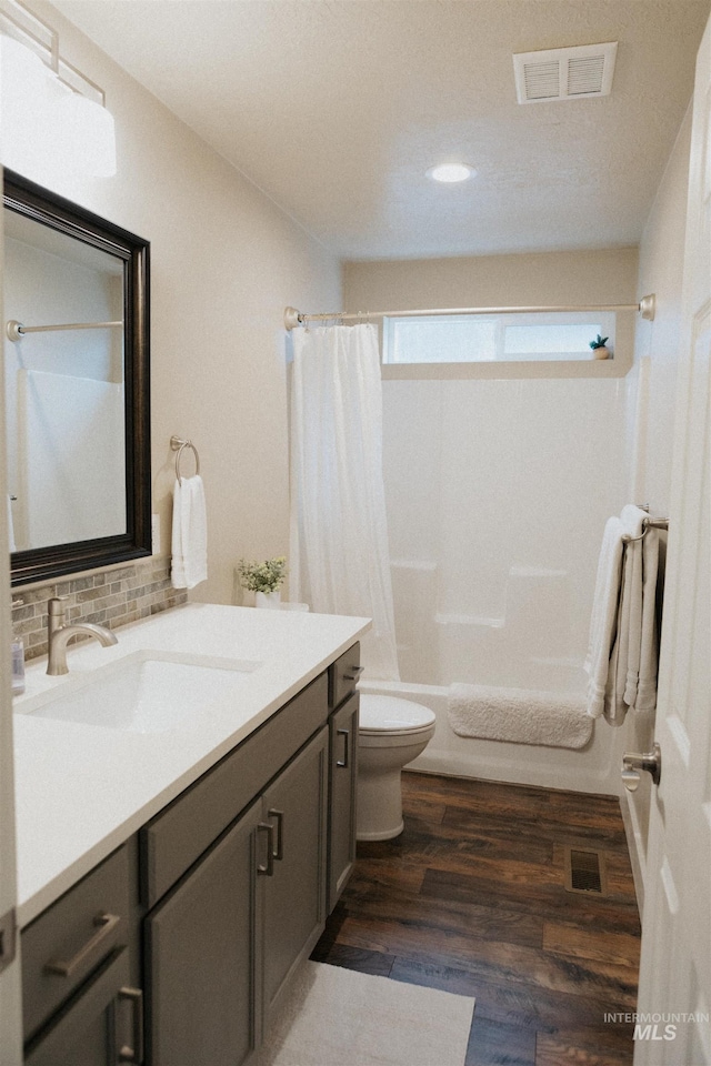 full bathroom featuring hardwood / wood-style flooring, shower / bath combo, vanity, tasteful backsplash, and toilet