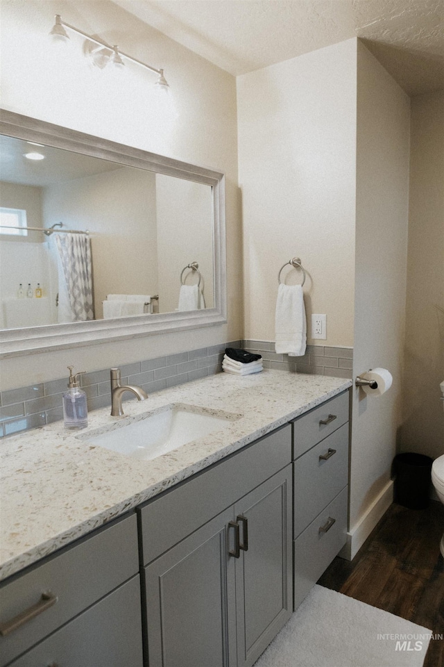 bathroom with hardwood / wood-style floors, backsplash, vanity, toilet, and a shower with curtain