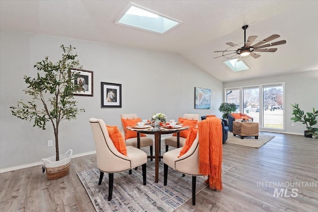 dining room with lofted ceiling with skylight, ceiling fan, baseboards, and wood finished floors