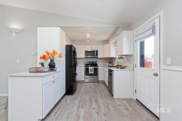 kitchen featuring light wood finished floors, light countertops, appliances with stainless steel finishes, white cabinetry, and a sink