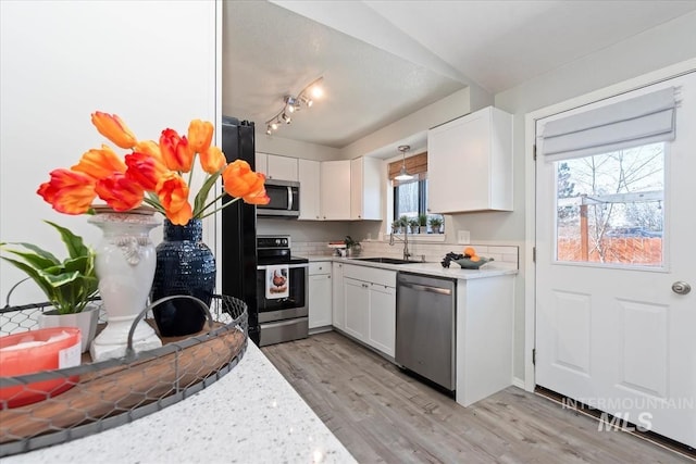 kitchen featuring light wood finished floors, stainless steel appliances, light countertops, white cabinetry, and a sink