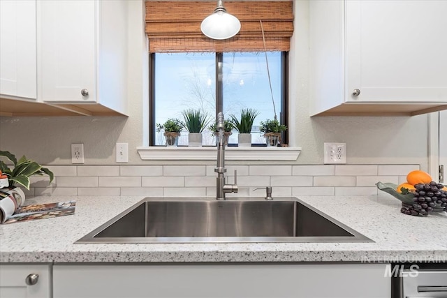 kitchen with light stone countertops, white cabinetry, and a sink