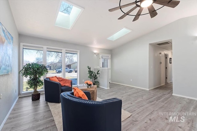 sitting room with visible vents, light wood-style floors, ceiling fan, vaulted ceiling with skylight, and baseboards