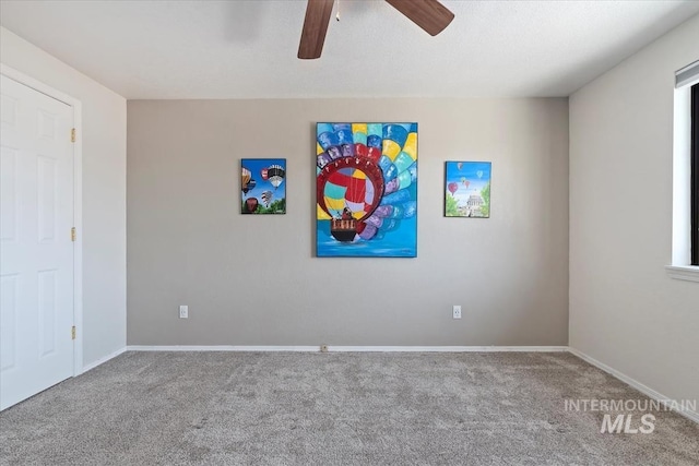 carpeted spare room with a ceiling fan and baseboards