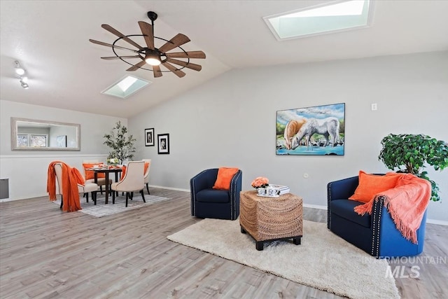 living area with ceiling fan, lofted ceiling with skylight, wood finished floors, and baseboards