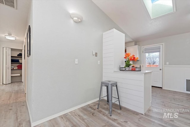 interior space with vaulted ceiling with skylight, visible vents, light wood-style flooring, and baseboards