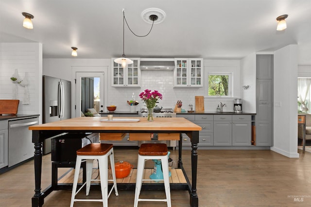 kitchen featuring decorative backsplash, glass insert cabinets, gray cabinets, a sink, and stainless steel appliances