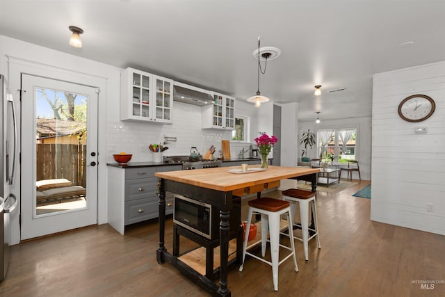 kitchen featuring decorative backsplash, butcher block countertops, dark wood-style floors, wall chimney range hood, and white cabinetry