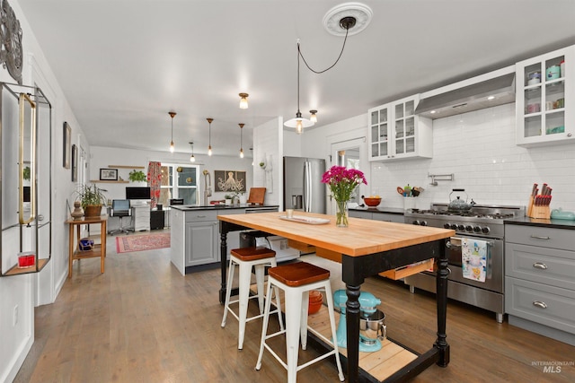 kitchen with decorative backsplash, custom exhaust hood, gray cabinets, wood counters, and appliances with stainless steel finishes