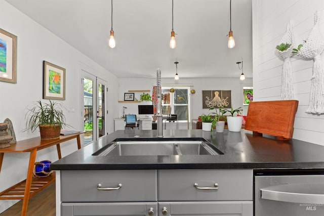 kitchen with stainless steel dishwasher, wood finished floors, dark countertops, open floor plan, and a sink