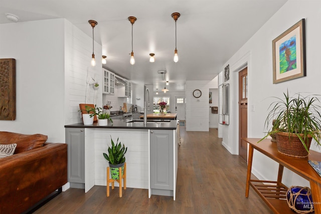 kitchen featuring a peninsula, dark countertops, glass insert cabinets, dark wood-style floors, and a sink
