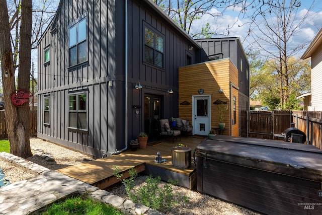 view of side of home featuring board and batten siding, a hot tub, fence, and a wooden deck