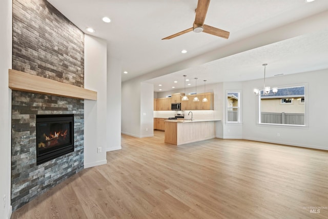 unfurnished living room featuring light hardwood / wood-style flooring, a large fireplace, and ceiling fan with notable chandelier