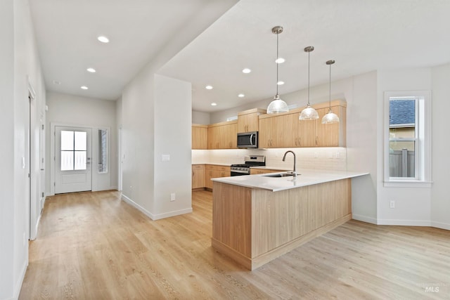 kitchen with kitchen peninsula, light hardwood / wood-style flooring, sink, pendant lighting, and stainless steel appliances