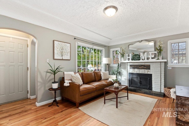 176 Taylor St, Twin Falls, ID 83301 - living room with a textured ceiling, healthy amount of natural light, light wood-style flooring, arched walkways, and a brick fireplace