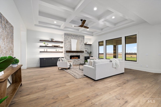 living room featuring coffered ceiling, a stone fireplace, ceiling fan, beam ceiling, and light hardwood / wood-style floors