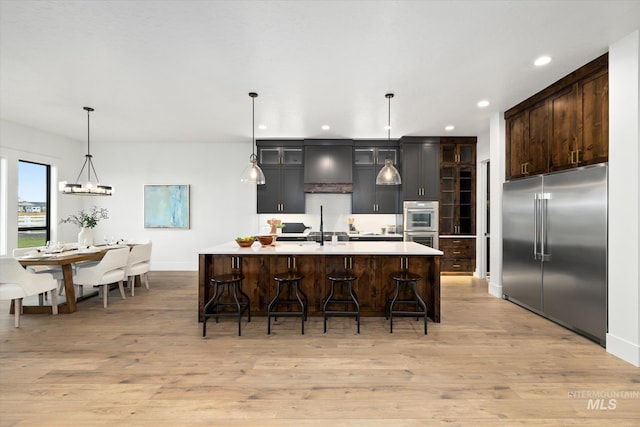 kitchen featuring appliances with stainless steel finishes, light hardwood / wood-style flooring, and an island with sink