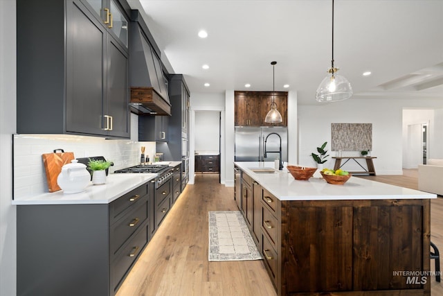 kitchen featuring pendant lighting, light hardwood / wood-style floors, stainless steel appliances, and a large island with sink