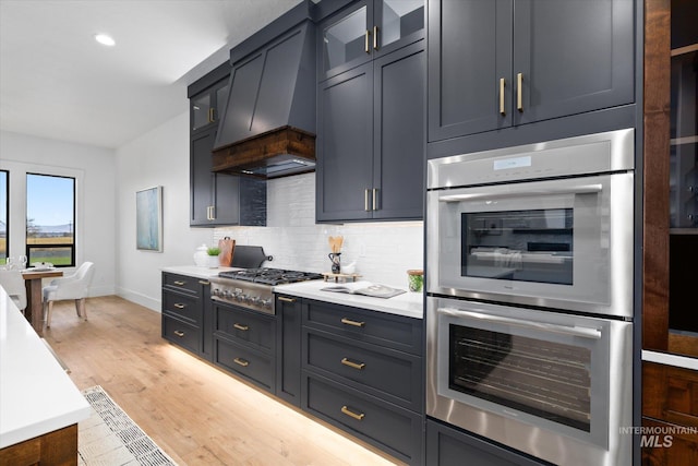 kitchen with backsplash, light wood-type flooring, premium range hood, and appliances with stainless steel finishes